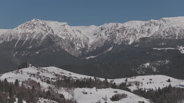 Cinematic forward aerial shot over a snowy plateau with rustic barns leading to Gaura Valley in the Bucegi Mountains, ungraded log