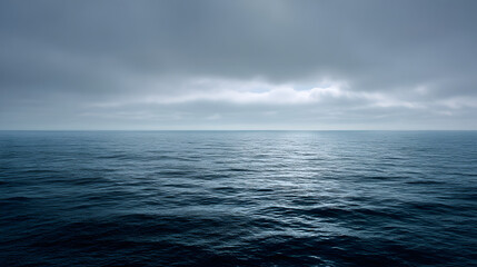 Obraz premium Dramatic and moody ocean landscape with dark blue rippling waves under a heavy overcast sky at dawn. Serene and atmospheric seascape with a clear horizon line.