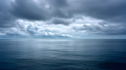 Obraz premium Dramatic moody dark ocean landscape under heavy storm clouds with soft light on horizon. Quiet blue sea background for meditation or atmospheric travel concepts.