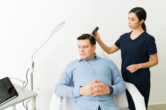 Hair specialist examining male patient scalp with trichoscope for hair loss diagnosis and treatment planning in clinic