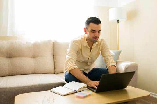 Young man freelancing from home, working remotely on laptop in a comfortable living room environment