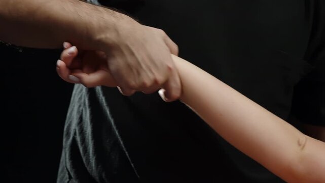 Close-up view of an adult hand firmly holding a child s forearm against a dark background, emphasizing the grip, skin texture, and contrasting tones in a tense, intimate moment