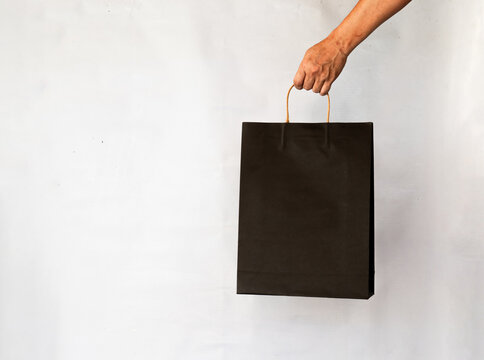 Hand holding paper shopping bag black color on white background.
