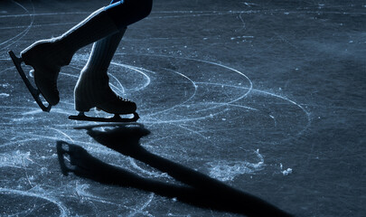 Close up of figure skater legs and blades on a shiny indoor ice rink with reflection and shadow....
