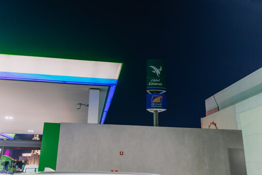Gas station at night with illuminated signage for Emirates and Adnoc, modern architecture and colorful lighting visible