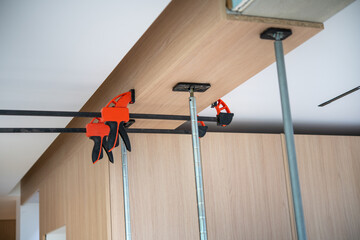 Wooden panel secured to ceiling with clamps and support poles