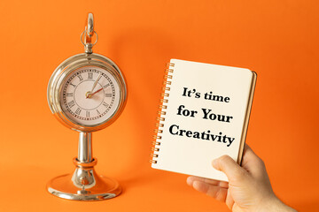It's time for Your creativity. Business and financial concept. Notebook with a slogan in hand. Stylish clock and beautiful orange background