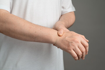 A man holding his wrist in discomfort, demonstrating symptoms of carpal tunnel syndrome against a...