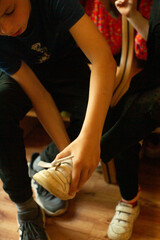 Obraz premium Brother helps sister put on shoes indoors. Children focus on fastening footwear during a daily routine. Child tying sneaker while seated closeup, velcro strap being fastened, hand detail and fingers