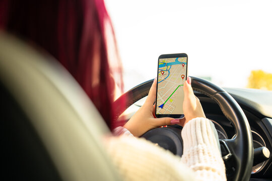 Young woman sitting inside a car, studying navigation on her smartphone with a concerned expression after getting lost in an unfamiliar city.