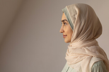 Side view of young Muslim woman wearing hijab, posing over light wall background studio profile portrait. Middle eastern Islam religious concept © Home-stock