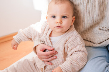 Cute baby wearing fleece sweater is sitting on mom, looking forward © glebzter