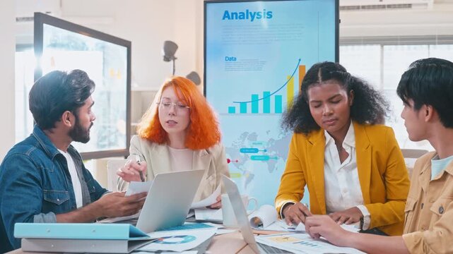 Diverse group of professionals focused on reviewing business analysis and digital data. Asian, Caucasian, and African American colleagues collaborating and discussing reports in a modern workspace