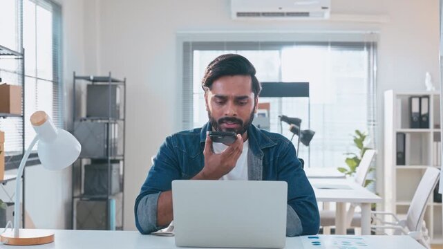 Indian man using AI voice assistant on smartphone in office, interacting with virtual assistant app for productivity, AI-powered speech, and smart technology.