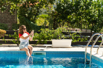 Freelance woman working remotely with a laptop and smartphone near a swimming pool