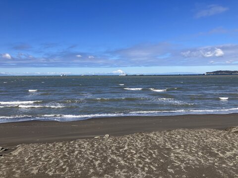 Gentle waves lap against the dark sandy shore of Tateyama Bay with a clear morning view of Mount Fuji on the horizon