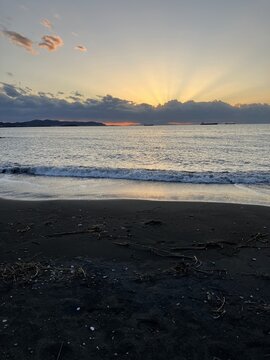 Crepuscular rays of the sun streaming through dramatic clouds over a dark sandy beach in Tateyama