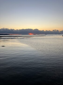 A serene coastal landscape at dusk with a crimson sunset glowing through thick clouds over the calm Tokyo Bay