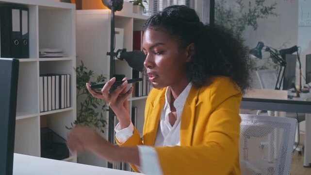 African American woman using an AI voice assistant on her smartphone in a modern office. Interacting with a virtual assistant app for enhanced productivity and AI-powered speech recognition