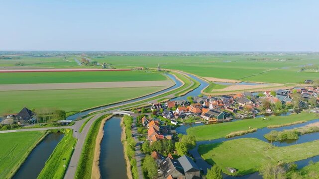 Stunning horizontal aerial overview of a rural Dutch village. Featuring traditional houses, narrow canals, and symmetrical agricultural fields. Authentic Holland landscape.