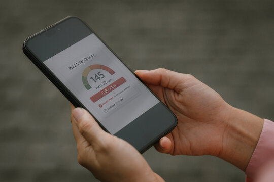 Close-up of a woman checking unhealthy air quality index on a smartphone app showing high PM2.5 levels, highlighting urban air pollution, environmental awareness, and health risk from toxic air.