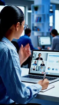 Focused businesswoman participates in a virtual team meeting on her laptop taking notes and analyzing data during a collaborative online conference call