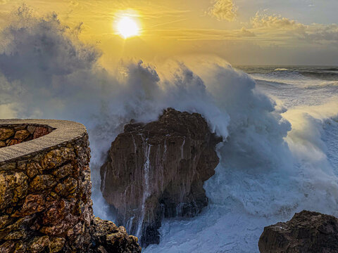 Golden sunset wave crashing into sea stack at Nazare Portugal