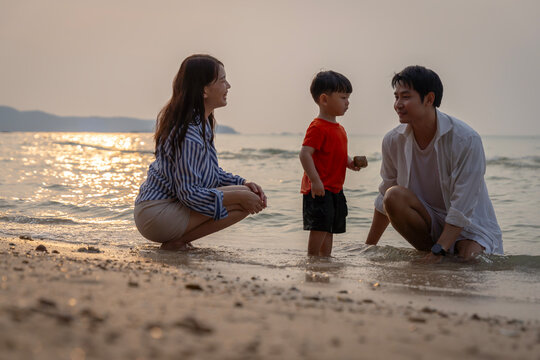 Happy Asian family with a young son enjoying sunset on the beach, playing in the sand and walking together during summer vacation.