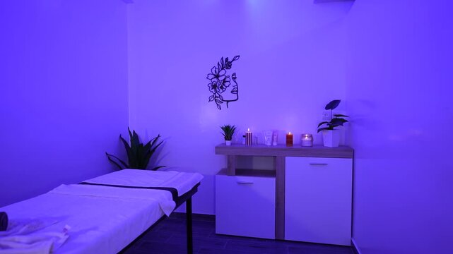 Int&eacute;rieur d'une salle de massage et spa relaxante avec &eacute;clairage d'ambiance violet, table de massage, bougies et serviettes.