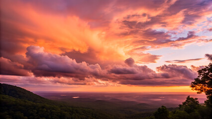 Fototapeta premium A beautiful sunset over the mountains and forest glows with dramatic orange and red light across a cloudy sky as the sun dips below the horizon in this stunning evening nature landscape view