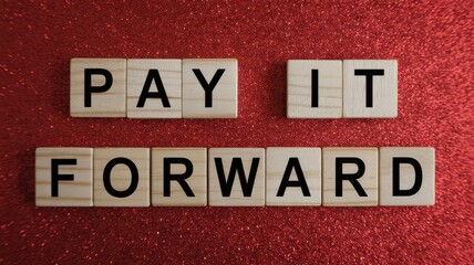 Obraz premium Vibrant photo of Pay It Forward Message with Wooden Letters on Red Glitter Background
