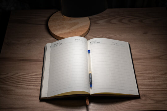 Open blank notebook on wooden desk under warm lamp light.