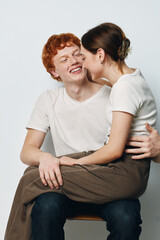 Young couple in casual clothes smiling and hugging with affection, sitting together on chair against white background in studio. Happiness, love and friendship moments.