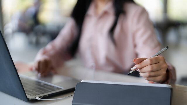 Blurred Asian adult woman working digital devices laptop tablet stylus multitasking online tasks remote work productivity creative design process business growth success