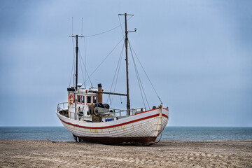 Obraz premium Beached Wooden Fishing Boats on Pebbled Shore Under Overcast Sky Along Calm Coastline, Slette Strand, Denmark