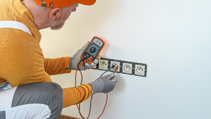 Electrical installation. The electrician's hands measure the voltage in an electrical outlet using a multimeter during installation a wall multi pack socket.