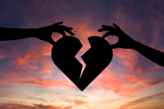 Hands holding broken heart against vibrant sunset sky