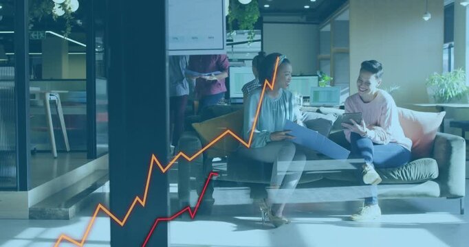 Two colleagues on sofa, right woman scrolling tablet causing business line charts rising for review