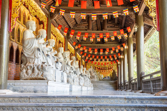 Row of arhat statues lining a temple corridor, decorated with buddhist and national vietnamese flags