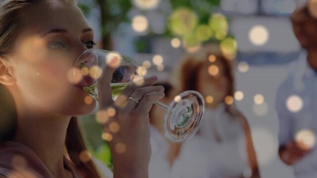 Woman lifting stemmed glass, sipping on patio for social hospitality, bokeh framing sip