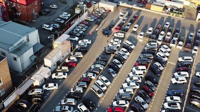 Aerial view of large urban parking lot densely packed with cars arranged in long parallel rows. Everyday mobility, commuting, city logistics