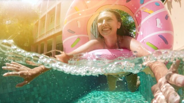 Young woman in blue swimsuit is swimming underwater in a pool, holding her breath and looking up at the surface while some air bubbles are coming out of her nose. Pretty girl with long hair is