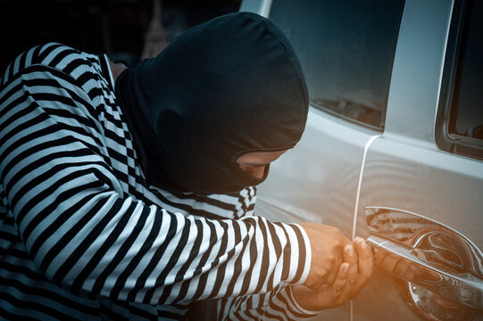 Car thief dressed in black striped trying to break into a car with a screwdriver.Car Robber dressed with a balaclava on his head try to unlock the door.Car thief stealing a car.