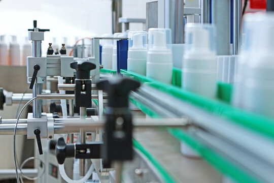 Conveyor belt for cosmetics production. A labeling machine. White plastic bottles without labels. Cosmetics production.