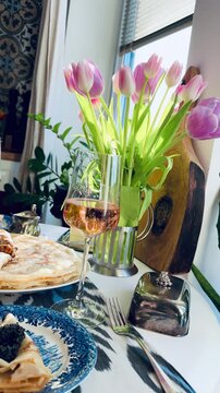 Luxury spring brunch celebrating Maslenitsa and March 8th. Festive table with pink Prosecco, black caviar, Perm ham, and crepes. Elegant holiday morning with purple tulips on ikat tablecloth.