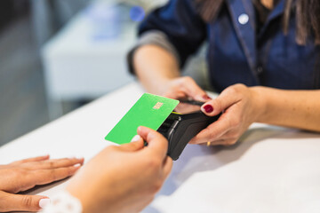 Fototapeta premium Woman holding green credit card tapping pos terminal at beauty salon checkout, contactless payment for service transaction and convenience