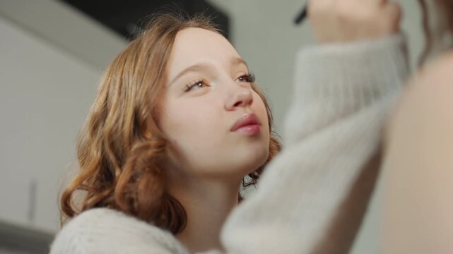 Youthful Makeup Session, Caucasian Adolescent Focused On Makeup Application In Warm Kitchen Setting, Teenager Concentrating On Eyeliner Technique While Wearing Soft Sweater In Kitchen Ambiance