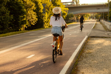 Back view of woman riding bike on path with trees lining the way, lady cycling on sunny day,...