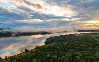 Fototapeta premium Panoramic aerial view of the Peruvian Amazon rainforest with dense green canopy stretching to the horizon. Morning mist rises from the tropical jungle as a winding river flows through the vast forest