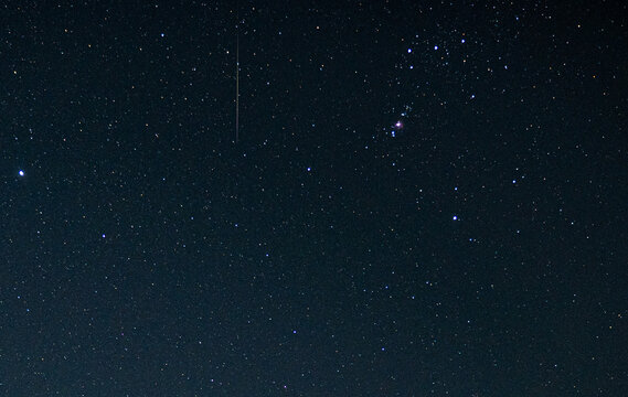 One meteor during geminid Meteor shower with other stars in the sky in the dark sky in which Orion nebula at bright side and one short light trail is meteor in the dark sky.